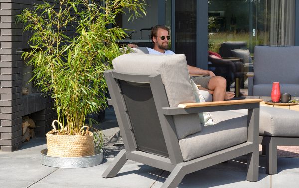 Man met zonnebril zit lekker op een tuinbank.